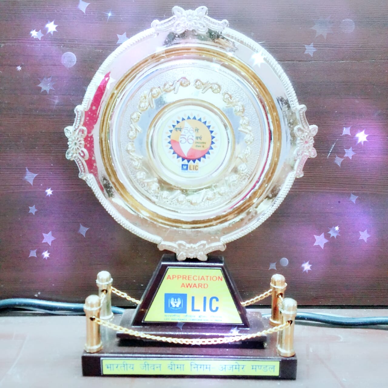 person writing in a notebook beside by an iPad, laptop, printed photos, spectacles, and a cup of coffee on a saucer