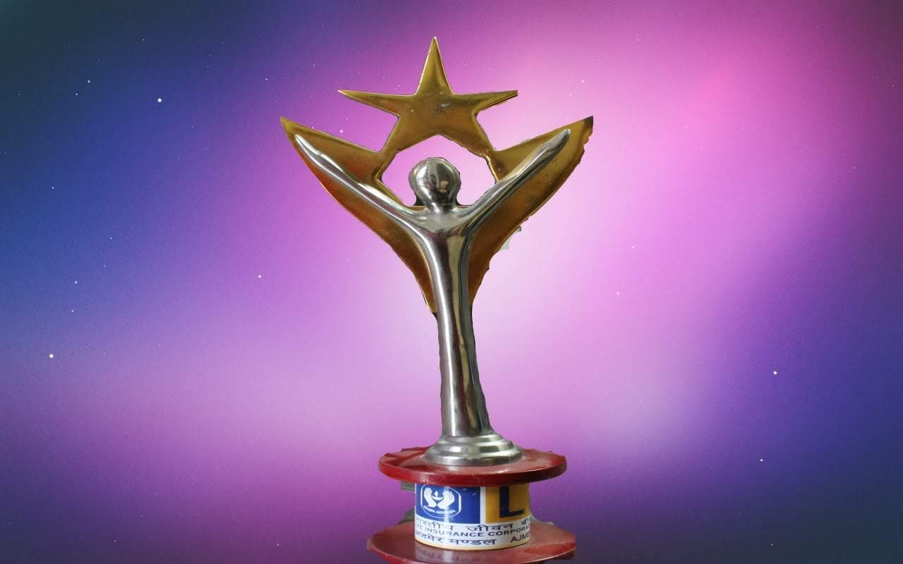 man wearing a black jacket, white shirt, blue jeans, and brown boots, playing a white electric guitar while sitting on an amp